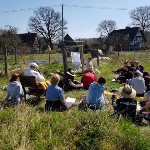 Powiększ obraz: uczestnicy słuchają prelegenta, siedzą na trawie